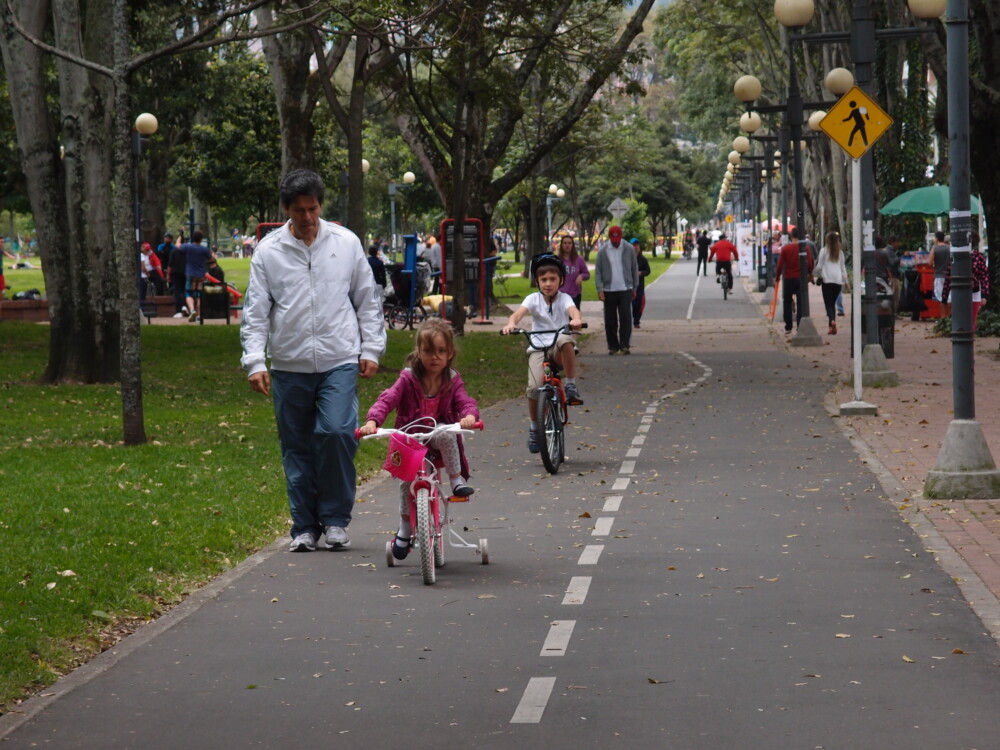 A man walking behind a young girl riding a bike in a bike path