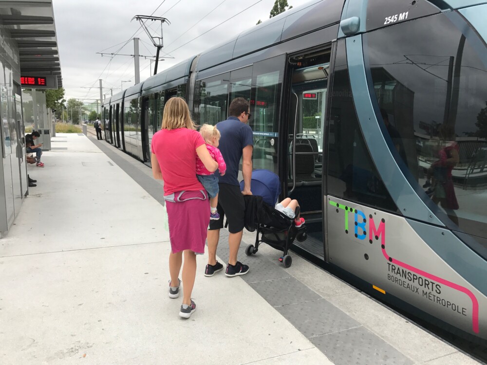A man boarding a train with a stroller and a woman holding a small child walking behind him